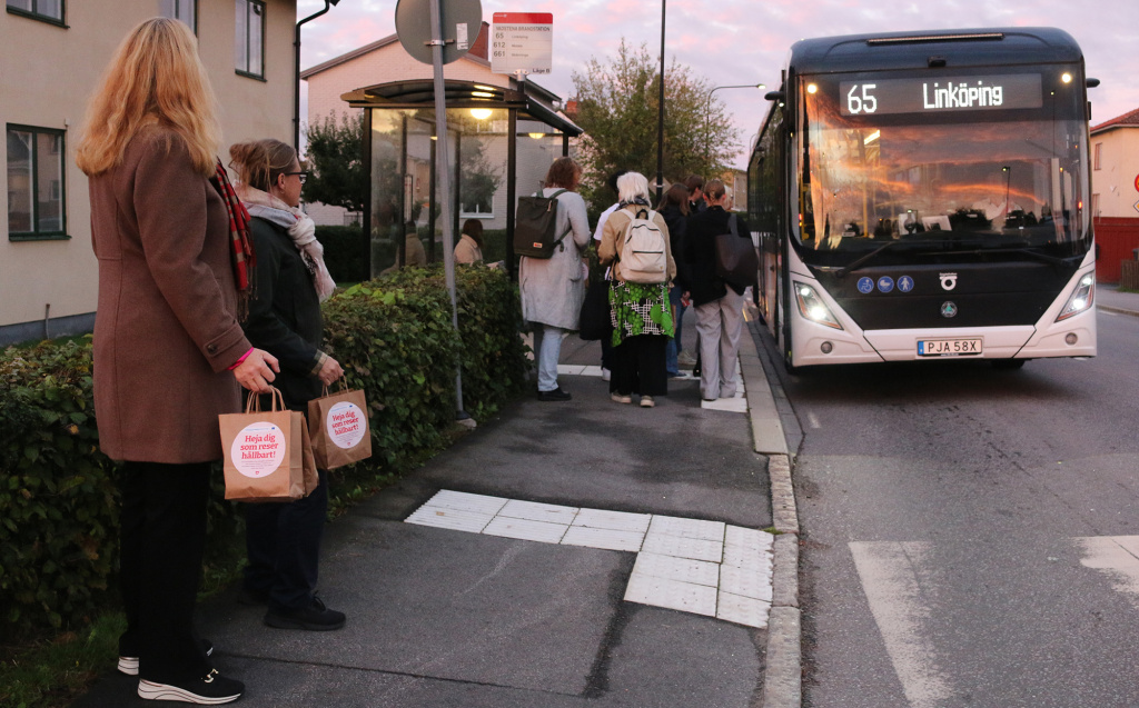 Buss stannar vid busshållplats med många människor.