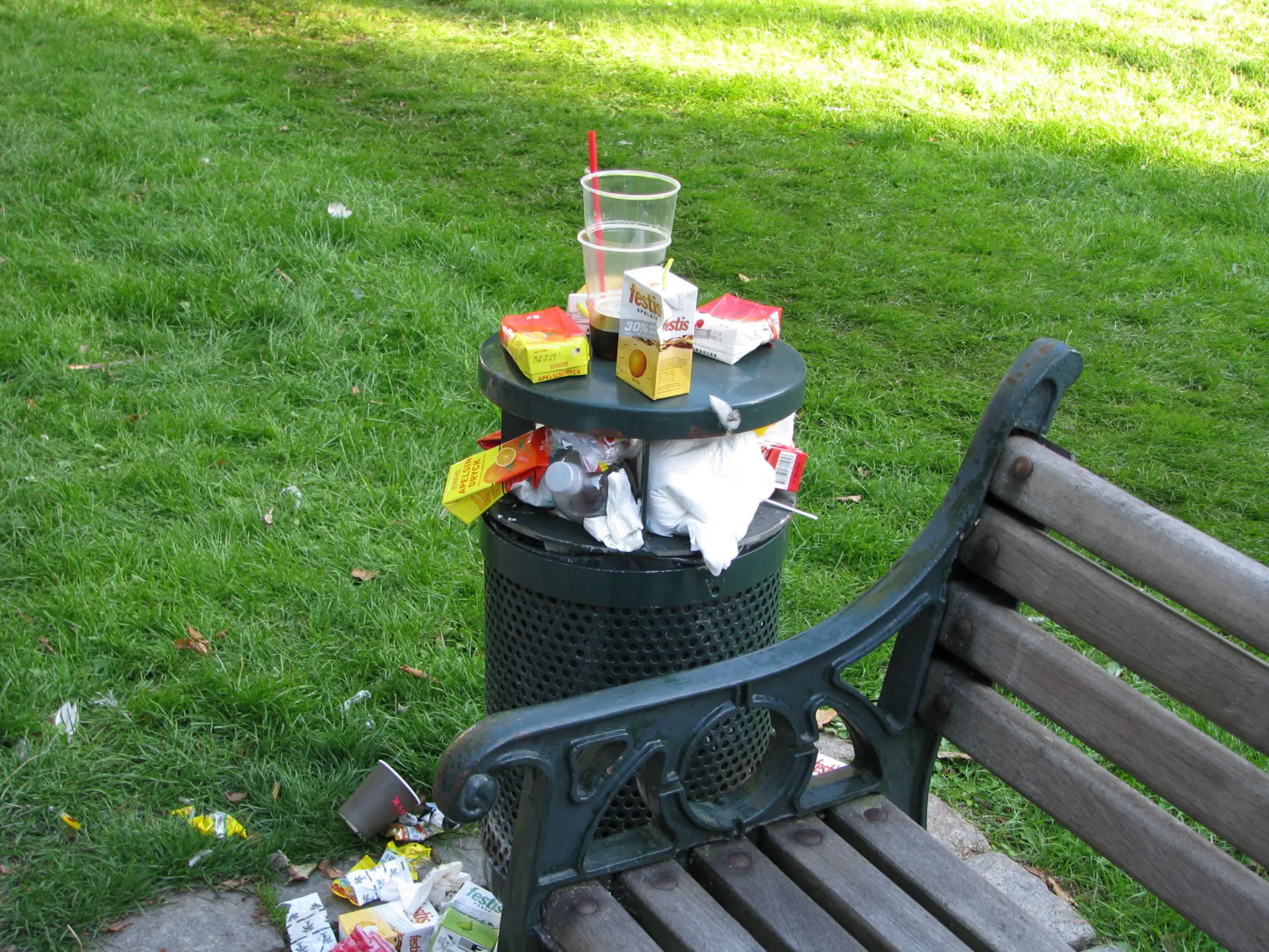 Överfull papperskorg intill parkbänk
