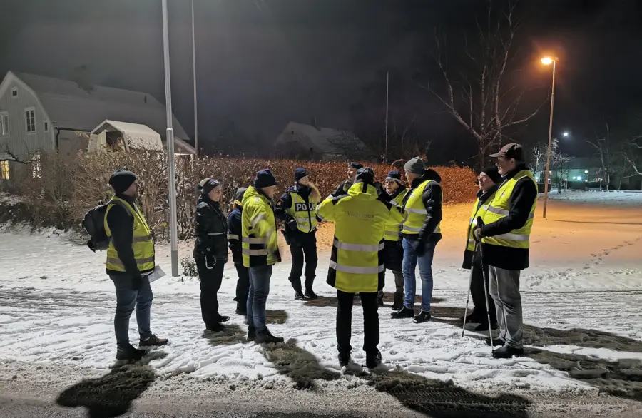 Grupp i reflexv&auml;star st&aring;r och diskuterar under gatlampa
