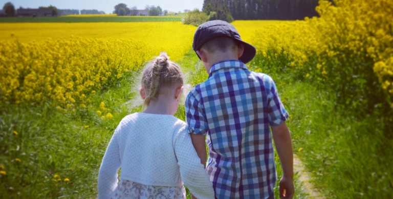 Syskon som går längs rapsfält