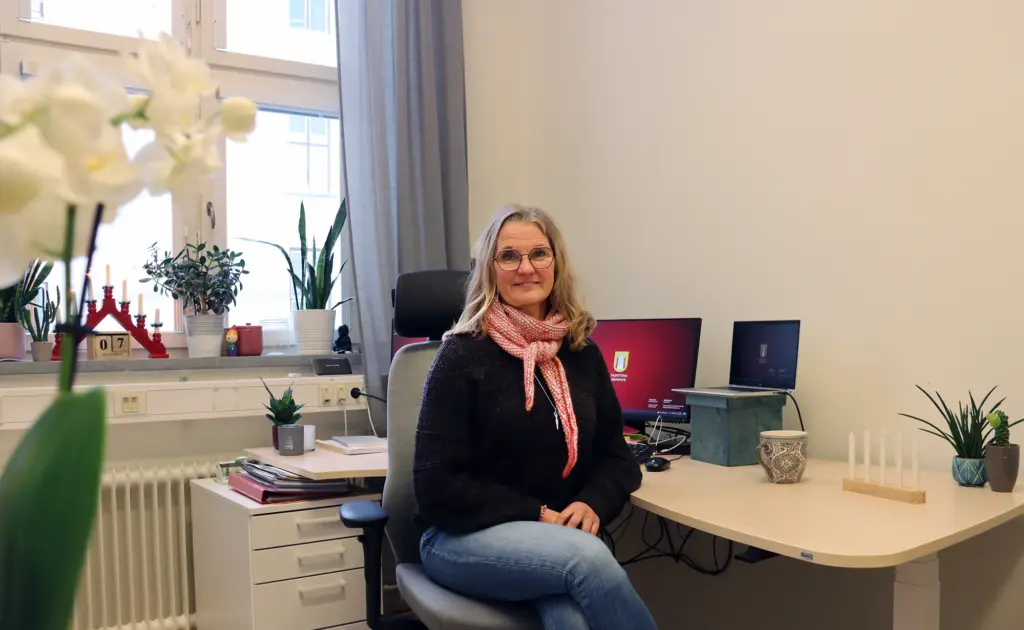 Marie Ziemke Larsson vid sitt skrivbord med fönster i bakgrunden.