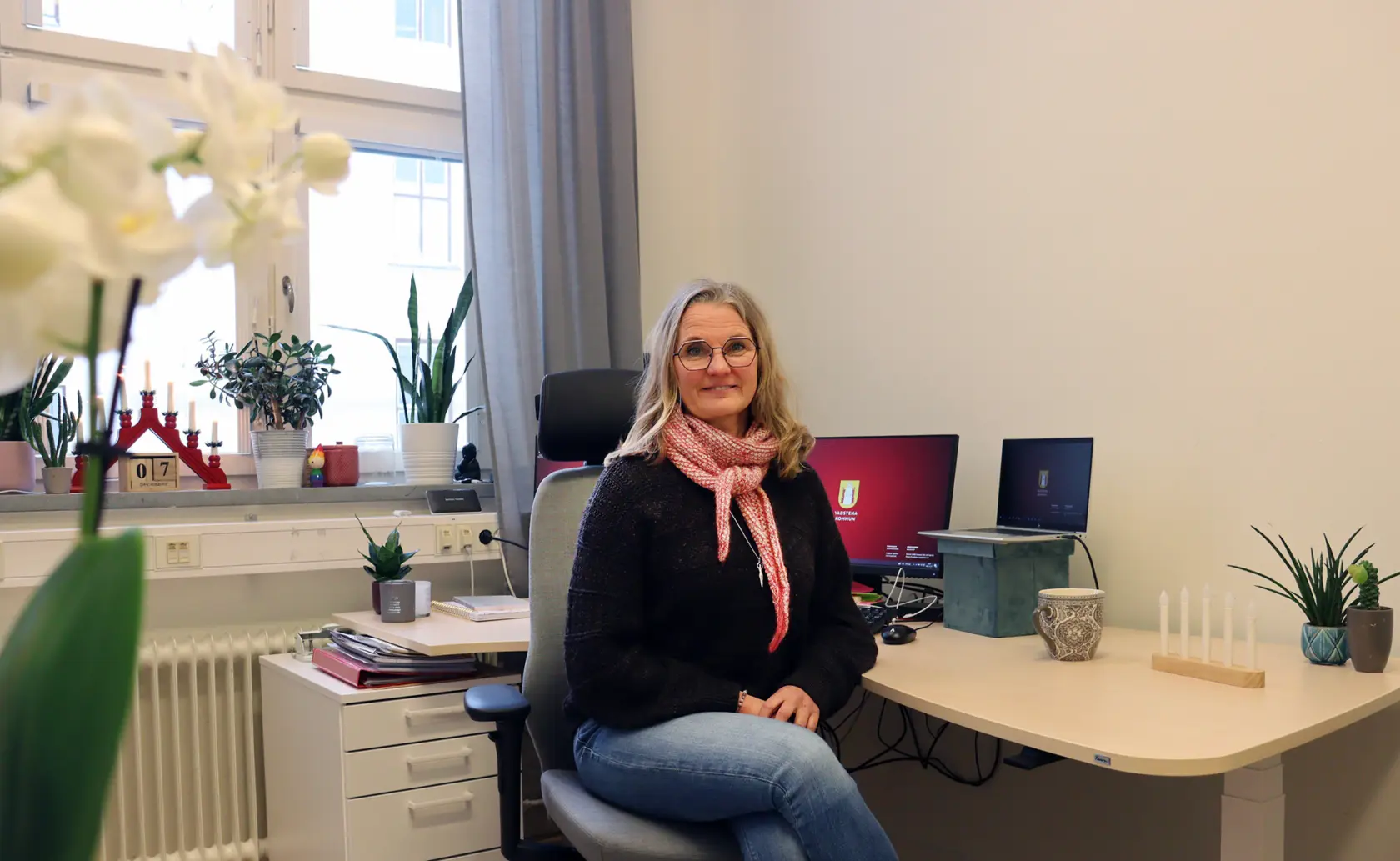 Marie Ziemke Larsson vid sitt skrivbord med fönster i bakgrunden.