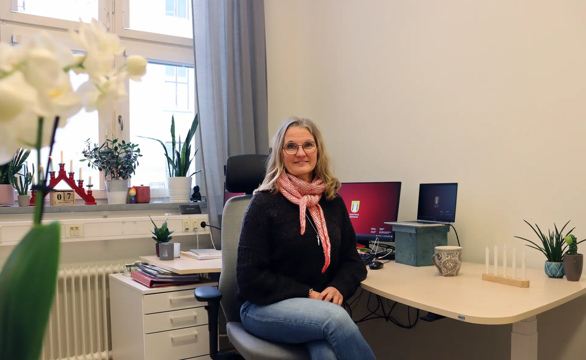 Marie Ziemke Larsson vid sitt skrivbord med fönster i bakgrunden.