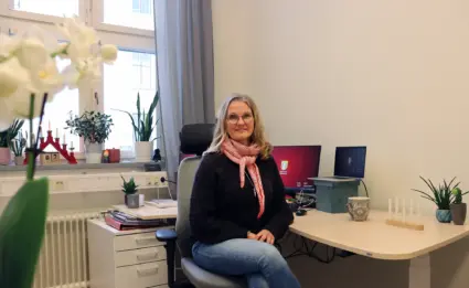 Marie Ziemke Larsson vid sitt skrivbord med fönster i bakgrunden.