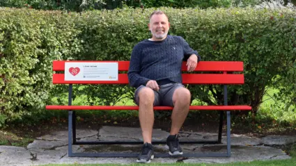 r´Richard sitter på bänk omgärdad av buskar