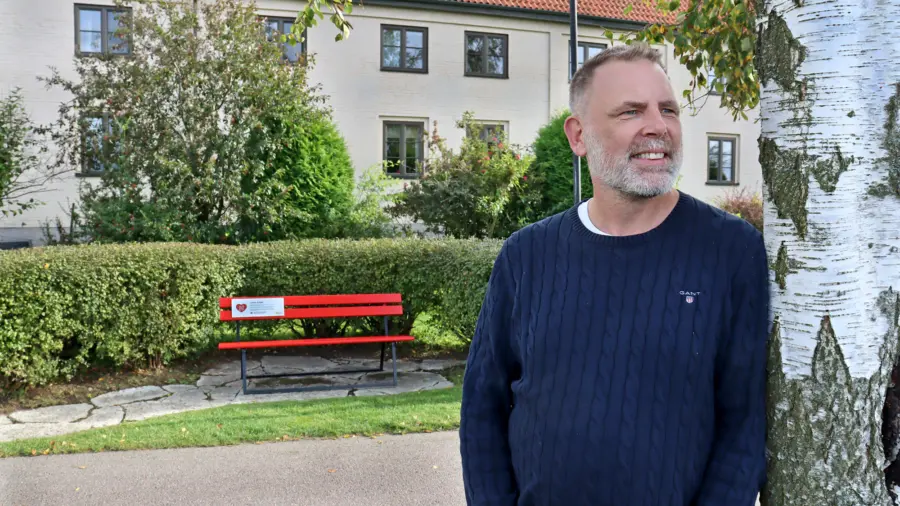 Rickard lutar sig mot björk, röd bänk syns i bakgrunden