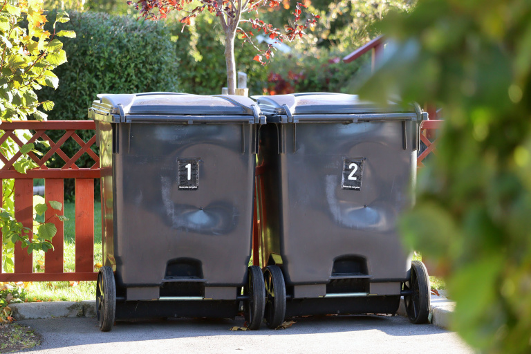 två soptunnor, fyrfackskärl vid rött staket
