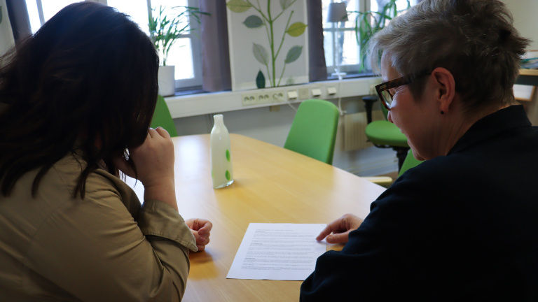 Två kvinnor sitter vid ett bord och pratar med ett papper framför sig.