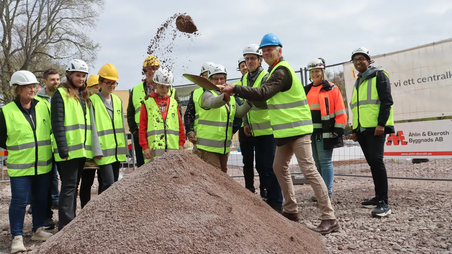 Grupp med människor tittar medan några tillsammans tar ett spadtag i en sandhög.
