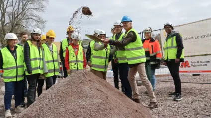 Grupp med människor tittar medan några tillsammans tar ett spadtag i en sandhög.