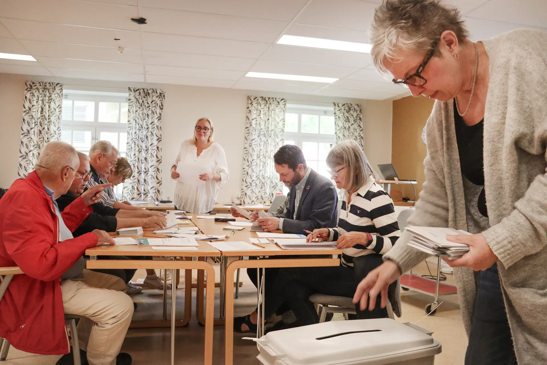 Människor som räknar röster kring ett bord medan en kvinna lägger ner röstkuvert i en plastbox.