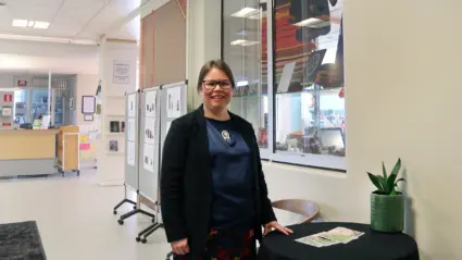 Kristina i biblioteket med samiskt hantverk bakom sig.
