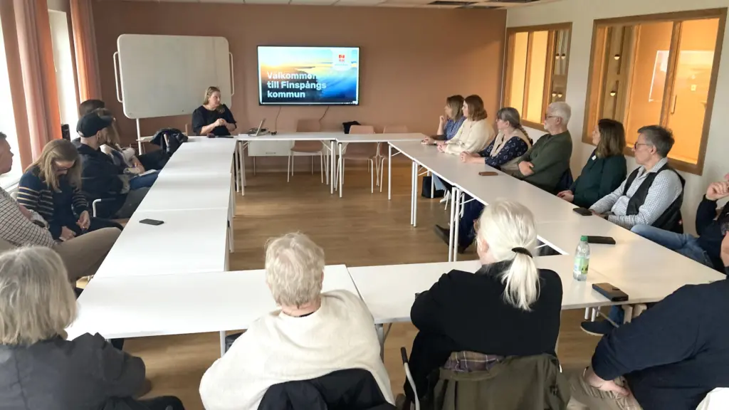 Människor kring bord i sammanträdesrum.