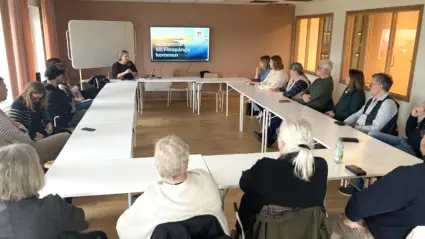 Människor kring bord i sammanträdesrum.