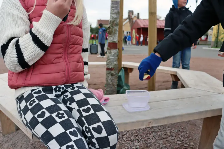 Flicka sitter på bänk på skolgården och äter frukt.