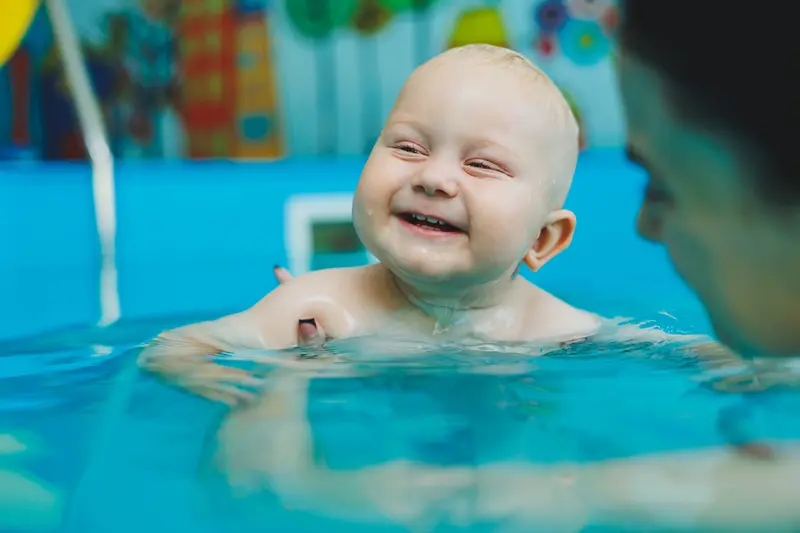Skrattande baby hålls av mamma i bassäng.