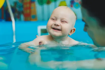 Skrattande baby hålls av mamma i bassäng.