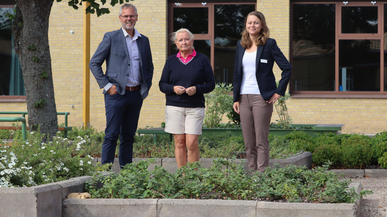 Tre personer uppställda bland planteringar på skolgården.