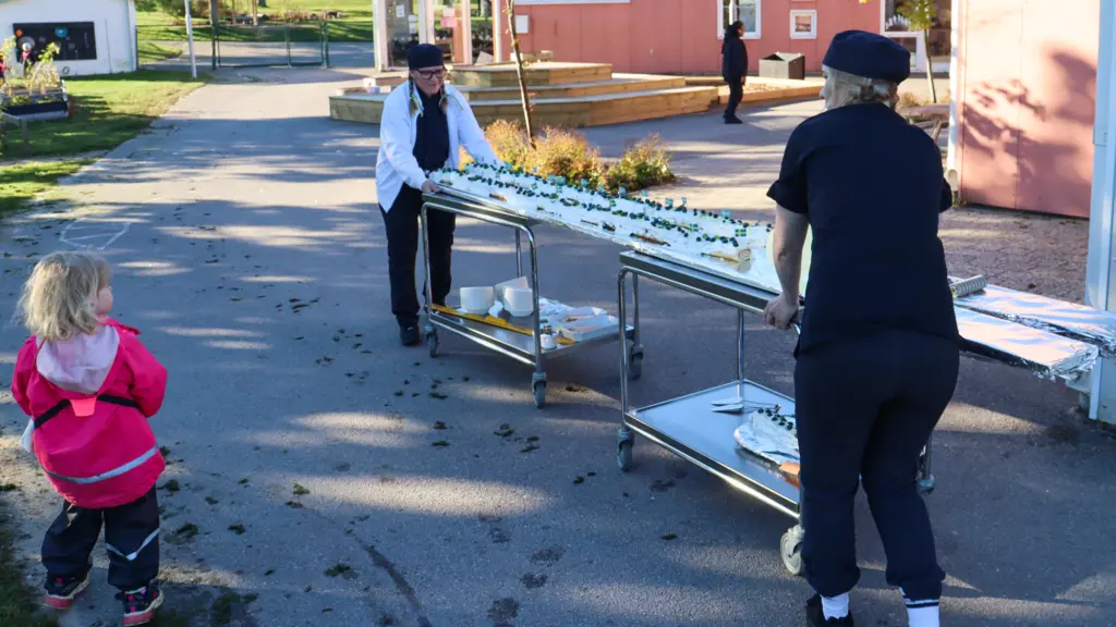 Två kockar drar ut lång rulltårta på vagn.