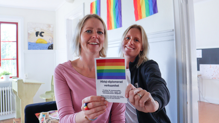 Kvinnor håller upp märke med info om HBTQI-diplomeringen.