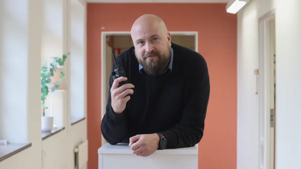 Johan lutar sig över en bänk med en kommunikationsapparat i handen.