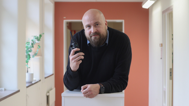 Johan lutar sig över en bänk med en kommunikationsapparat i handen.