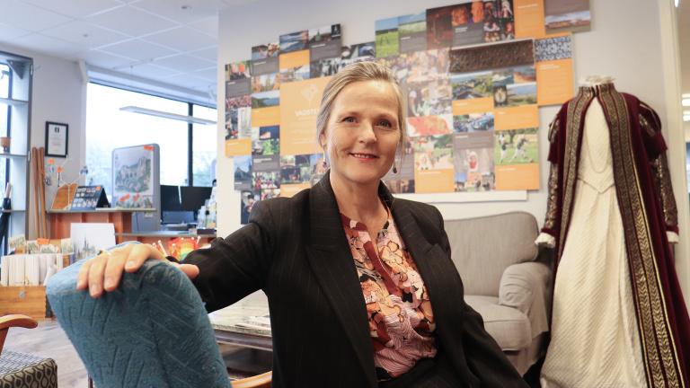 Stina sitter i en fåtölj med turistinformation på väggen bakom.