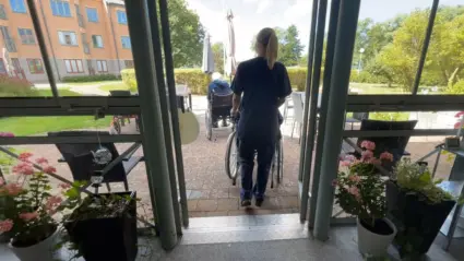 Vårdanställd skjuter en rullstol ut genom en dörr.