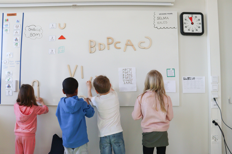 Fyra barn skriver på whiteboard i klasrum.