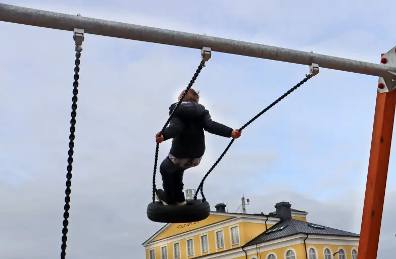 Ett barn som gungar med skolan i bakgrunden.