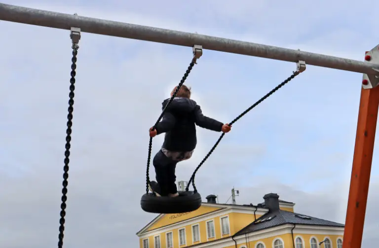 Ett barn som gungar med skolan i bakgrunden.